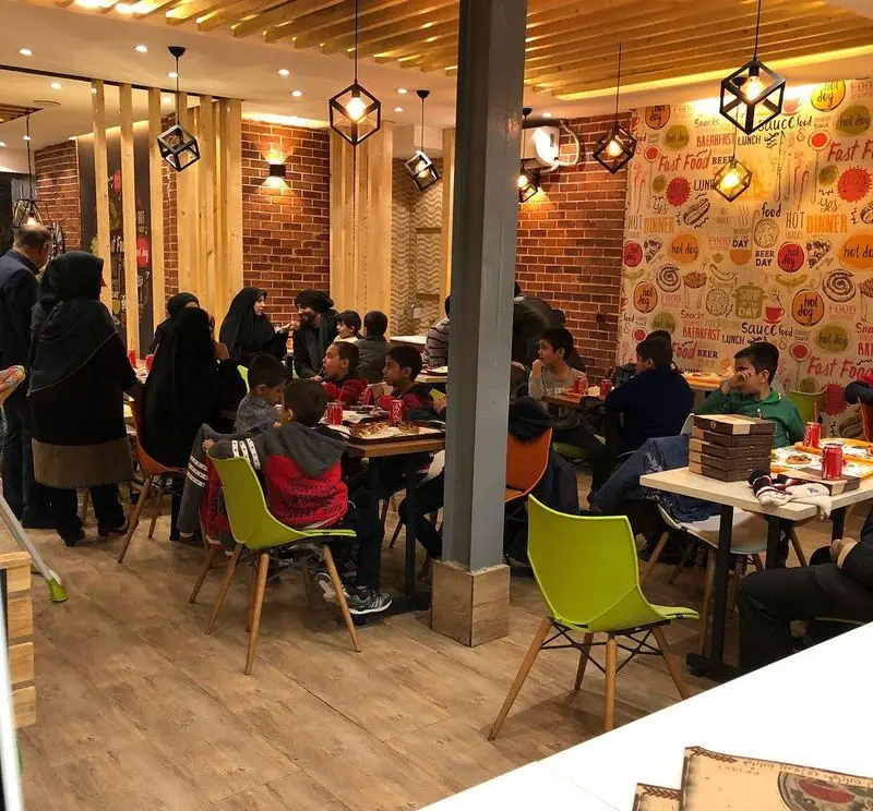 تصویری از فضای داخلی شلوغ پیتزا تنوری پاروت؛ مشتریان خانواده و کودکان مشغول صرف پیتزا در محیطی دوستانه با دکوراسیون جذاب.