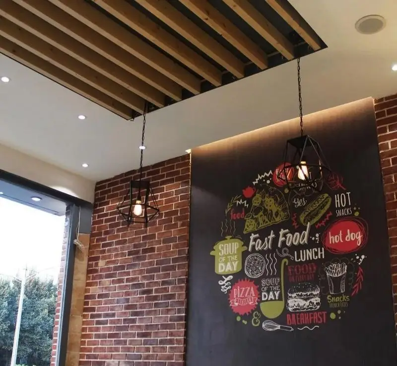 دکوراسیون داخلی مدرن پیتزا تنوری پاروت با دیوارهای آجری، سقف چوبی و تابلوی فست فود با طرح پیتزا و هات داگ.
