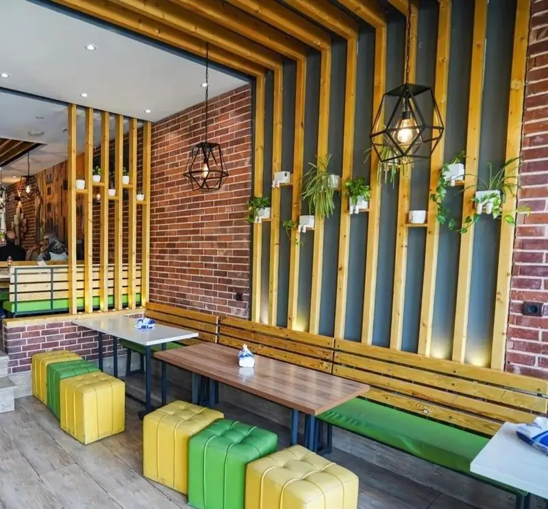 دکوراسیون داخلی مدرن و جذاب پیتزا تنوری پاروت با دیوارهای آجری، چوب‌های تزئینی، نشیمن‌های سبز و زرد، فضای دلنشین رستوران