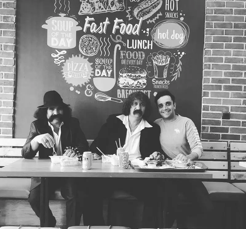 مشتریان شاد در پیتزا تنوری پاروت؛ دیوار منوی فست فود، پیتزا، سوپ روز و اسنک دکور شده، فضایی دوستانه برای صرف غذا.