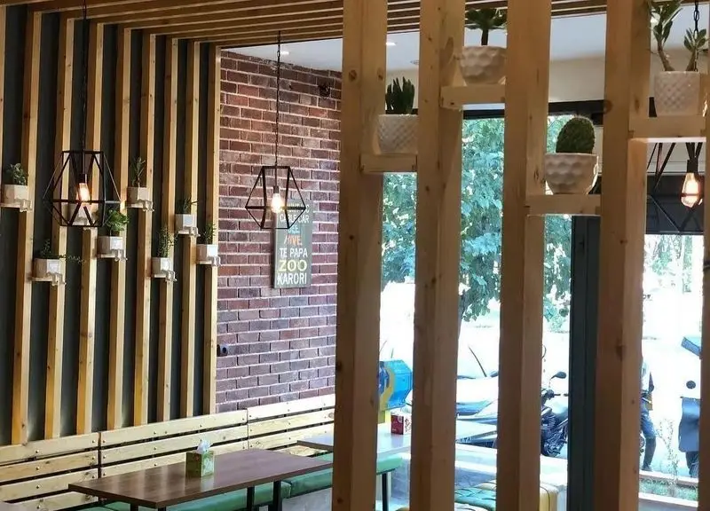 فضای داخلی دکوراسیون مدرن پیتزا تنوری پاروت شامل دیوار چوبی و آجری، نورپردازی خاص، گلدان‌های سبز و نشیمن راحت برای تجربه دلپذیر.