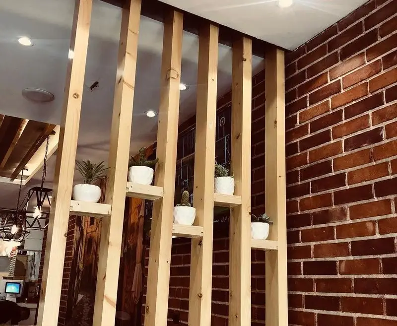 دکوراسیون داخلی مدرن و دلنشین پیتزا تنوری پاروت با دیوارهای آجری، پارتیشن چوبی و گلدان‌های سبز، فضایی گرم و دعوت‌کننده برای مشتریان.