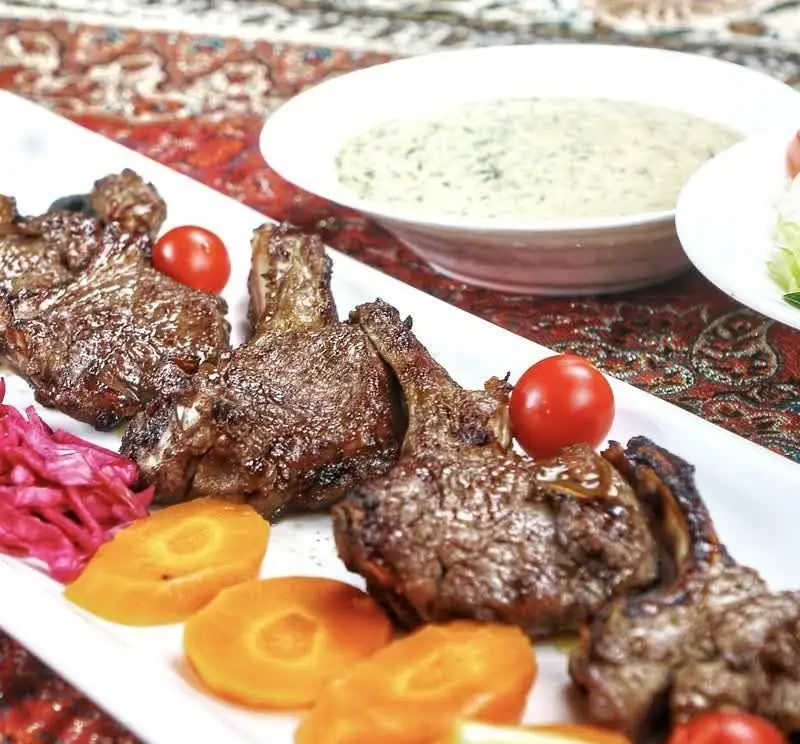 شیشلیک لذیذ و کباب دنده گوسفندی در رستوران VIP پویا، با تزئین گوجه گیلاسی، هویج و کلم قرمز. تجربه غذایی اصیل ایرانی.