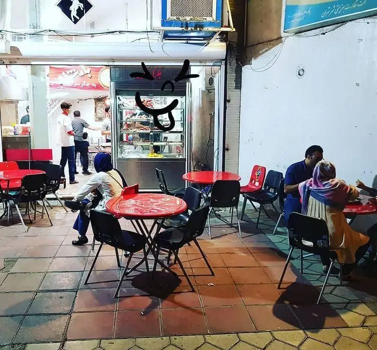 تصویری از جگرکی بامشاد در شب: مشتریان در فضای باز و داخل مشغول غذا خوردن هستند. محیطی صمیمی و دلنشین برای صرف انواع جگر و کباب.