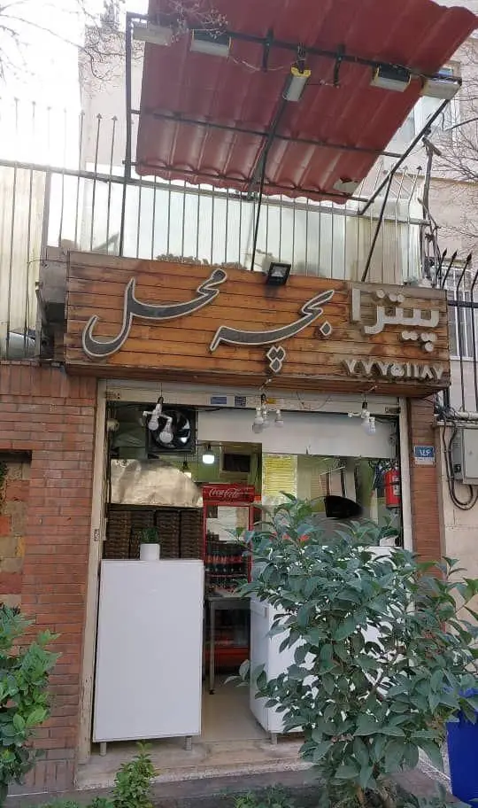 تصویر نمای بیرونی پیتزا فروشی "بچه محل" با تابلوی چوبی برجسته و سایبان قرمز، ورودی مغازه فست فود آماده خدمات رسانی.