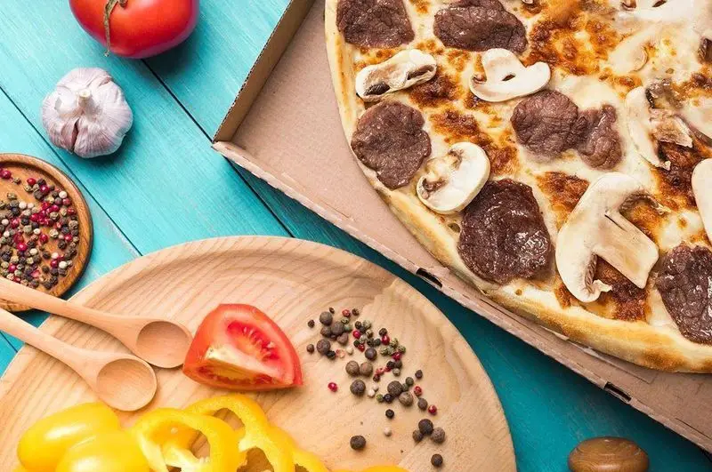 پیتزا گوشت و قارچ تله پیتزا (شعبه‌ی پیروزی) با مواد اولیه تازه، از جمله گوجه، فلفل دلمه‌ای و ادویه‌جات رنگی، آماده سرو.