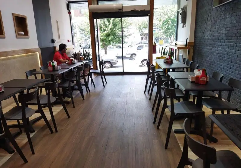 تصویری از فضای داخلی دنج و مدرن تله پیتزا شعبه پیروزی با چیدمان مرتب میز و صندلی‌های شیک، کفپوش طرح چوب و نورگیر عالی.