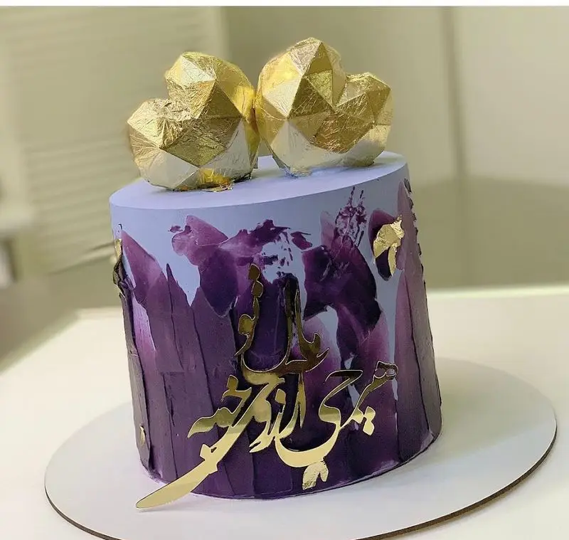 کیک مدرن بنفش و ارغوانی با تزئینات طلایی، شامل دو قلب هندسی و کالیگرافی برجسته، از شیرینی سرای شکلات تهرانپارس.