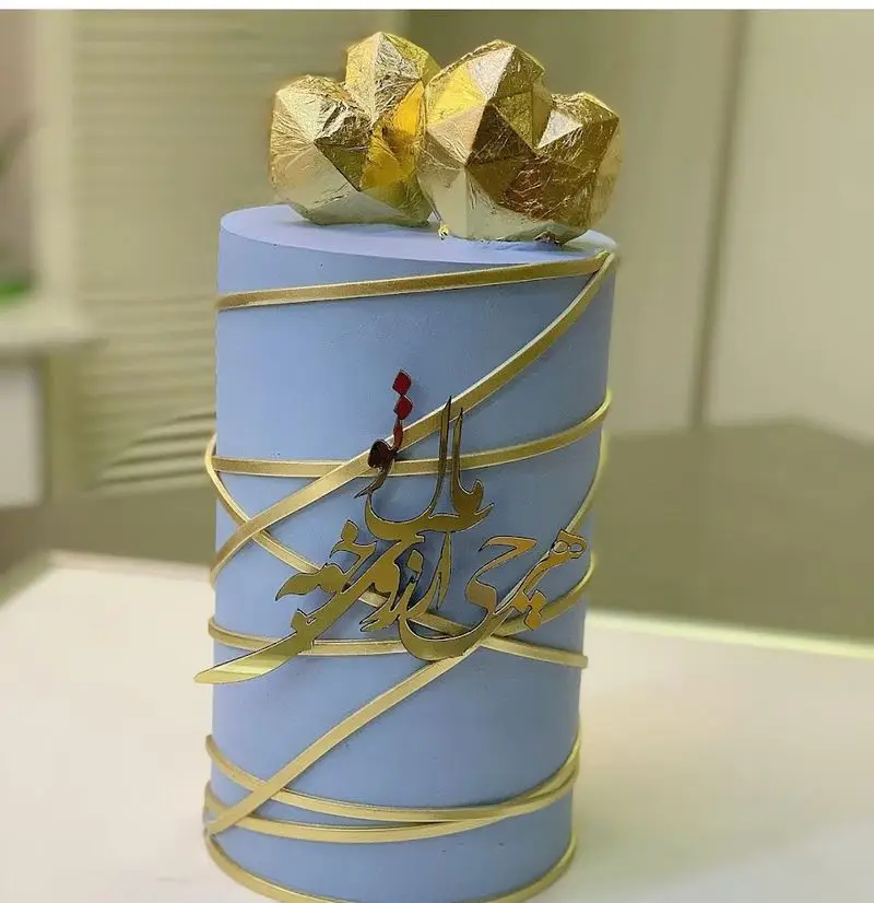 کیک مدرن آبی رنگ با خطاطی طلایی و تزیینات هندسی قلب، انتخابی لوکس از شیرینی سرای شکلات تهرانپارس برای مناسبت‌های خاص.