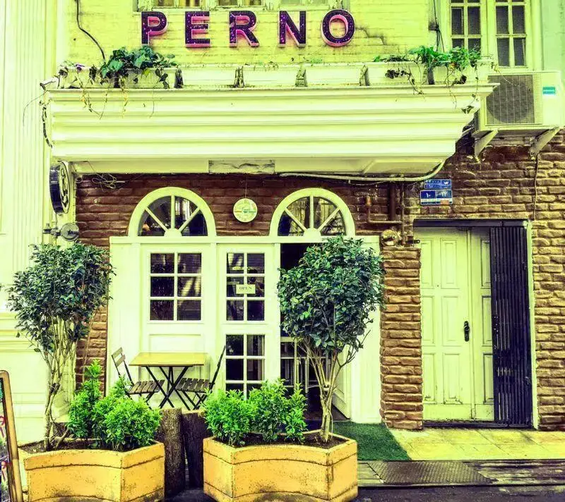 ورودی رستوران ایتالیایی پرنو با تابلوی PERNO، گلدان‌های سبز، میز کافه و درب و پنجره‌های چوبی زیبا.