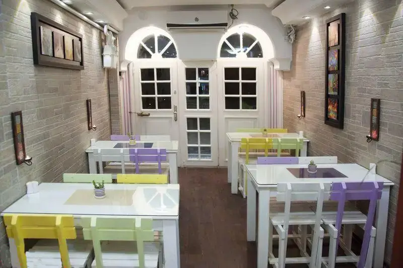 فضای داخلی دلنشین و شیک رستوران ایتالیایی پرنو با میزهای سفید شیشه‌ای، صندلی‌های رنگارنگ پاستلی و دکوراسیون مدرن.