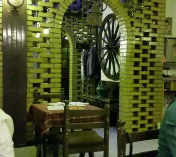 فضای داخلی دنج پیتزا پنتری با دیوارهای آجری سبز، طاق‌های قوسی، میز و صندلی چوبی، و چرخ درشکه قدیمی تزئینی.