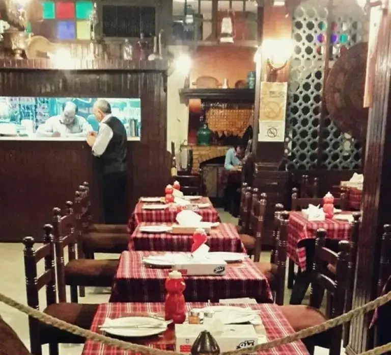 تصویری از فضای داخلی رستوران پیتزا پنتری با دکوراسیون چوبی و سنتی. میزهای آماده سرو غذا با رومیزی شطرنجی، و کارکنان در حال خدمت رسانی.