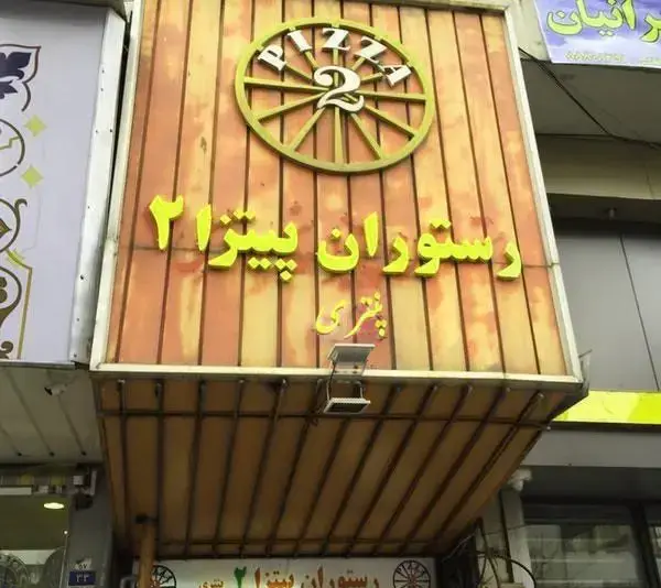 تابلو ورودی رستوران پیتزا پنتری با طرح چوبی، نمایش دهنده نام "پیتزا ۲" و "پنتری" با لوگوی جذاب چرخ پیتزا.