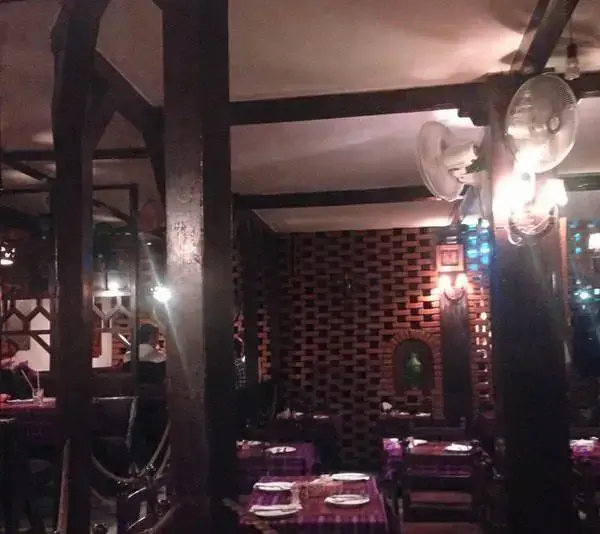 فضای داخلی دلنشین رستوران پیتزا پنتری با ستون‌های چوبی، دیوار آجری تزئینی و میزهای چیده شده در محیطی دنج و آرام.