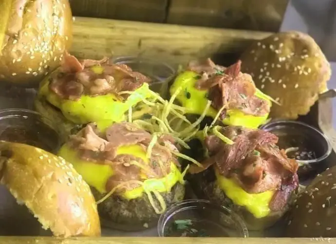 تصویر نزدیک از چند مینی برگر لذیذ فست فود تاپاس فودبار با پنیر زرد، بیکن و پیاز ترد طلایی روی سینی چوبی.