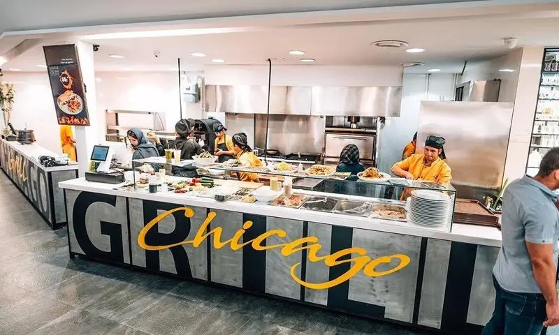 نمای کامل فست فود شیکاگو گریل، شامل کانتر بزرگ سرویس با لوگوی شیکاگو، غذاهای تازه و متنوع، و پرسنل فعال در آشپزخانه مدرن