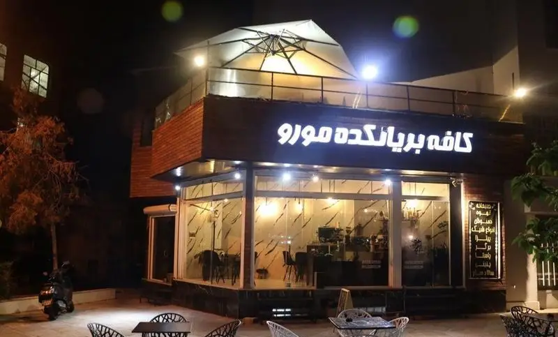 تصویری از کافه بریانکده مورو در شب، با نورپردازی زیبا، روف‌گاردن با چتر، فضای باز و داخلی دنج، منوی متنوع نوشیدنی، قهوه و غذا.