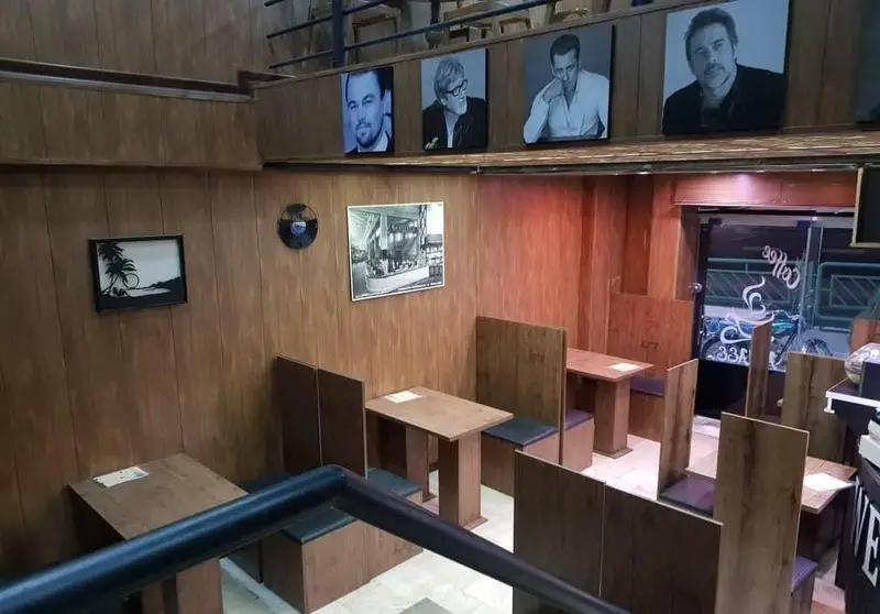 فضای داخلی کافه آریایی، با دیوارهای چوبی، میزهای دنج و تابلوهای هنری از جمله پرتره مشاهیر و صحنه‌های قدیمی.