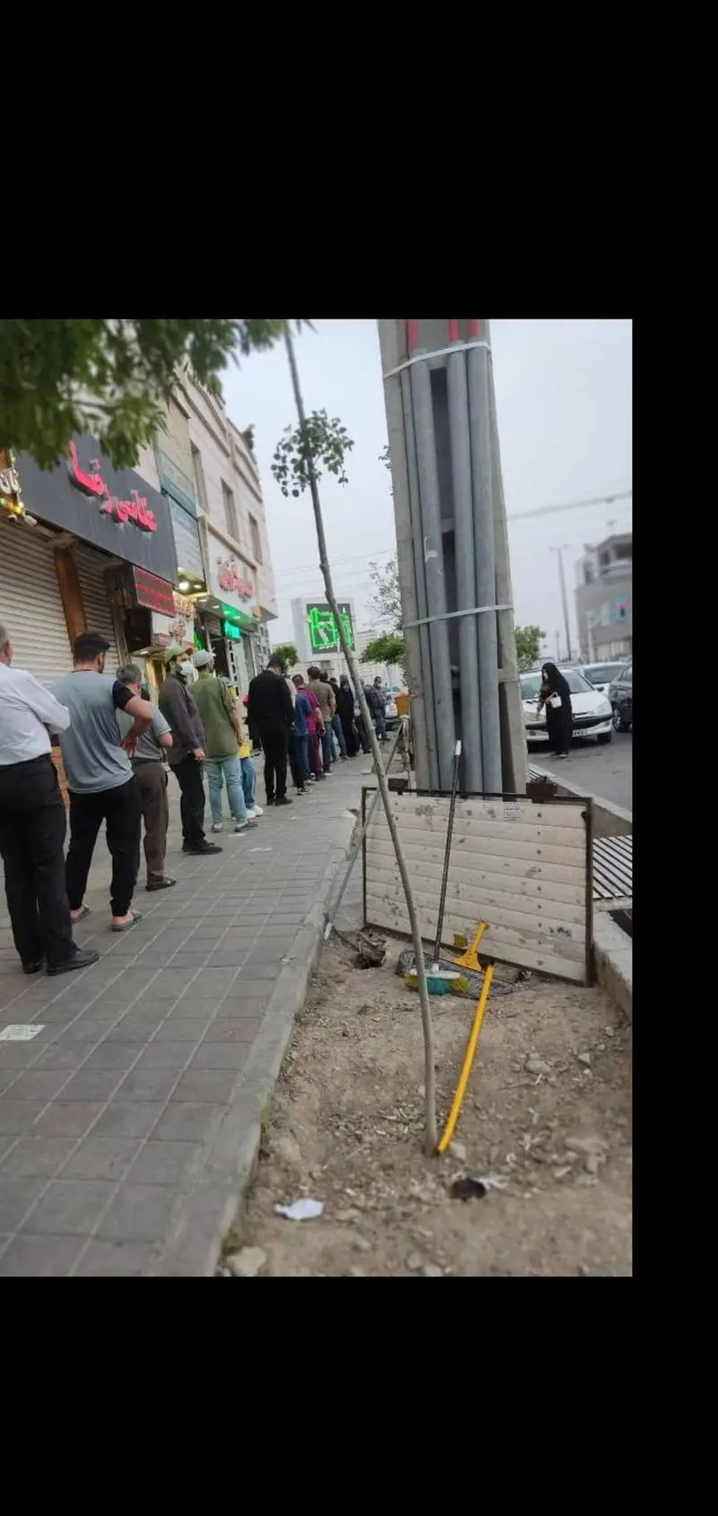 صف بلند مشتریان در پیاده‌روی شلوغ، منتظر دریافت حلیم تازه و باکیفیت از حلیم فرزین در یک روز ابری.