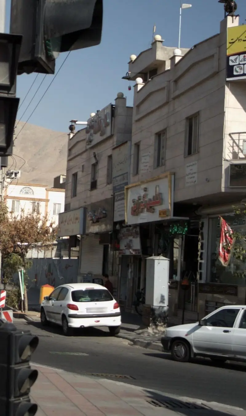 نمای بیرونی مغازه حلیم فرزین در خیابانی شلوغ با مردم، ماشین‌ها، و ساختمان‌های شهری در روز روشن.