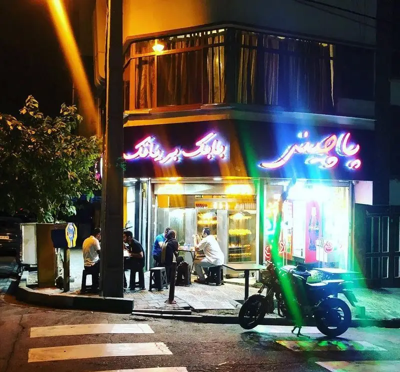 تصویری شبانه از نمای بیرونی رستوران بابک بریانک با تابلوی نئون درخشان. مشتریان از غذای سنتی بریانک در فضای باز لذت می‌برند.