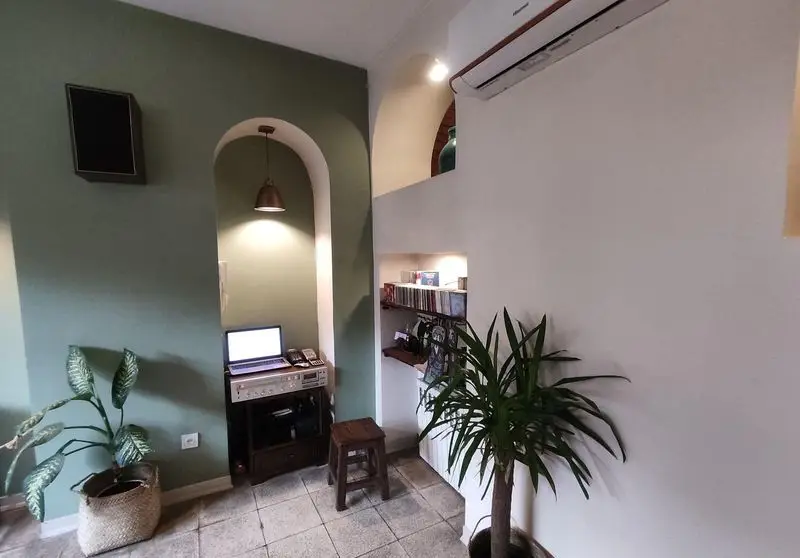 نمایی از فضای داخلی دنج کافه خانه میرا با طاقچه‌های سنتی، میز کار، سیستم صوتی و گیاهان آپارتمانی. مکانی ایده‌آل برای آرامش و موسیقی.