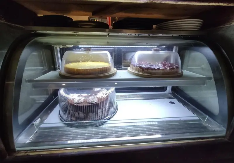 ویترین کیک کافه خانه میرا: چیزکیک لیمویی، چیزکیک توت‌فرنگی و کیک شکلاتی تازه و خوشمزه آماده سرو به مشتریان کافه.