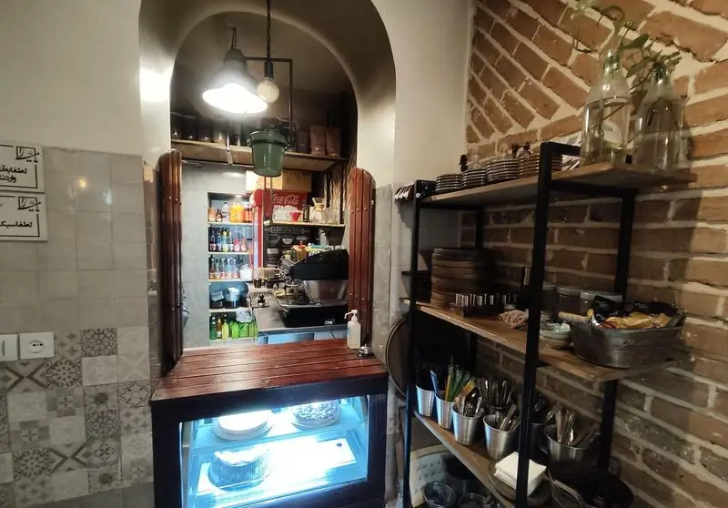 تصویری از دکوراسیون داخلی کافه خانه میرا، شامل کانتر سرو، یخچال کیک، دستگاه اسپرسو و قفسه‌های زیبا با ظروف و دکوریجات. فضایی گرم و دلنشین.