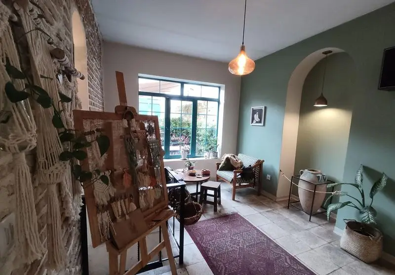 فضای داخلی دنج و هنری کافه خانه میرا با دکوراسیون بوهو، شامل دیوار مکرومه، استند صنایع دستی و نور طبیعی در کافه ای آرام.