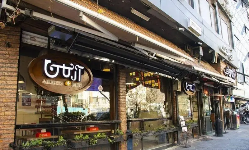 تصویری از نمای بیرونی کسب و کار ساندویچ آرمن در خیابانی شلوغ، با تابلوی بزرگ و نورانی "آرمن پلاس" و ویترین‌های شیشه‌ای.