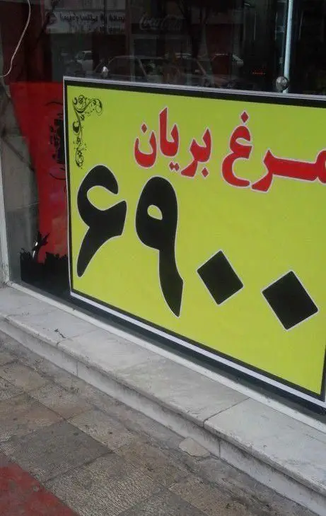 تبلیغ مرغ بریان پیتزا یمک با قیمت ۶۹۰۰ تومان روی تابلوی زرد رنگ در ویترین، گزینه ای عالی برای ناهار یا شام.