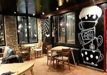 فضای داخلی جذاب و دنج کافه اسفند با دکوراسیون خاص دیواری، نقاشی بزرگ فنجان قهوه و دیوار چوبی در محیطی شیک.