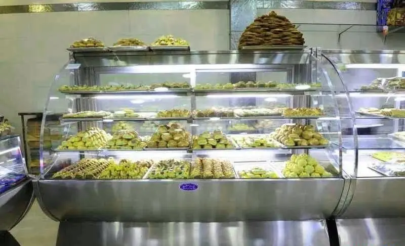 ویترین بزرگ و جذاب یک فروشگاه شیرینی‌ با آرایشی دلنشین از انواع شیرینی‌های تازه و باکیفیت، شامل شیرینی دانمارکی اصیل و دسرهای خاص.