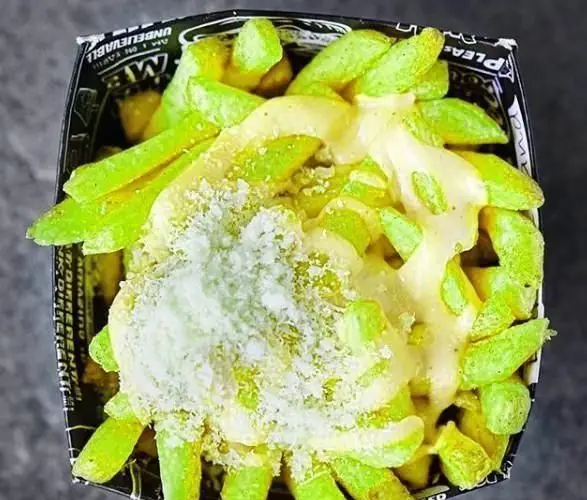 تصویری نزدیک از سیب زمینی سرخ کرده سبز و پنیری ویژه برگرلند، غرق در سس پنیر و تزئین شده با پنیر پارمزان. طعم خاص فست فود برگرلند.