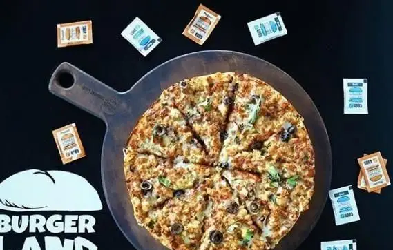 پیتزا پرملات و خوشمزه برگرلند با تاپینگ گوشت، قارچ و زیتون روی تخته چوبی، همراه با سس‌های مخصوص فست فود برگرلند.