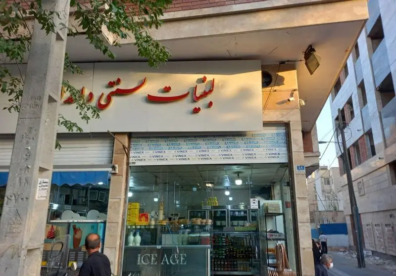 نمای کلی از مغازه لبنیات سنتی دامداران با تابلو برجسته قرمز و محصولات لبنی تازه در ویترین شیشه ای آماده عرضه به مشتریان.