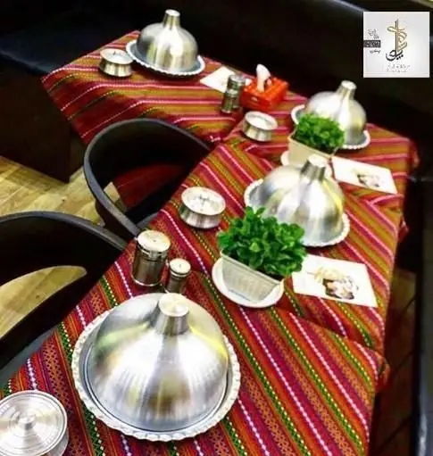 میزهای زیبای رستوران ایرانی پلو شاهی نیوان با رومیزی سنتی، ظروف آلومینیومی و گیاهان تزئینی، آماده میزبانی مهمانان