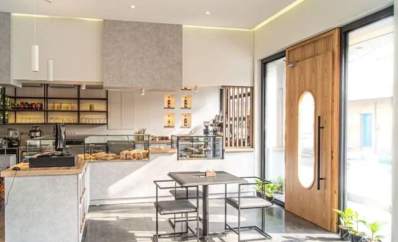 داخلی کافه بردوتی با دکوراسیون مدرن و روشن، پیشخوان پر از شیرینی و قهوه، میز و صندلی برای مشتریان، درب ورودی چوبی شیک، و فضای دلنشین و آرامش‌بخش.