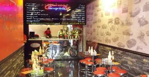 تصویر فضای داخلی رستوران و کافه گاراژ گریل با دکوراسیون منحصر به فرد شامل پیشخوان، موتورسیکلت تزیینی و میزهای شیک.