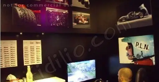 دکوراسیون منحصر به فرد گاراژ گریل با تم ریسینگ، شامل تصاویر خودروهای مسابقه، رینگ و کلاه ایمنی. مشتری در حال تجربه فضای بازی.