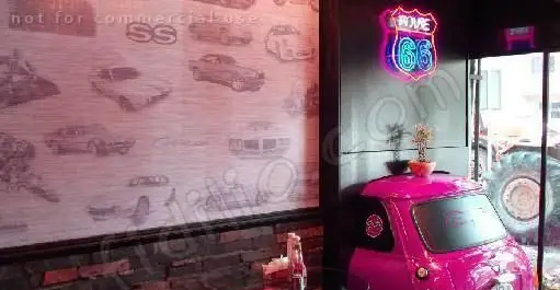 دکوراسیون داخلی گاراژ گریل با تم ماشین‌های کلاسیک و تابلوی نئون روت ۶۶. ماشین صورتی و دیوار طرح خودروها فضایی منحصر به فرد ایجاد کرده است.