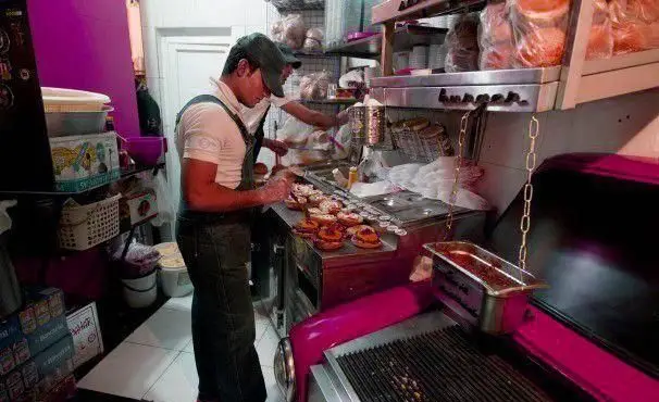 تصویری جذاب از آشپزخانه فعال و پویای گاراژ گریل، جایی که پرسنل با دقت برگرهای خوشمزه را آماده و سرو می‌کنند. این فست فود آماده پذیرایی از مشتریان است.