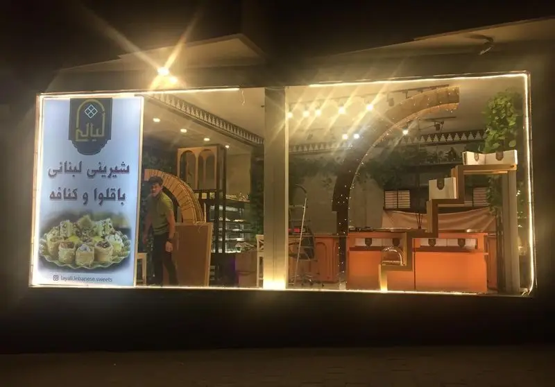 نمای شبانه شیرینی فروشی لیالی، یک فروشگاه شیرینی لبنانی با تابلو باقلوا و کنافه و دکوراسیون داخلی روشن.