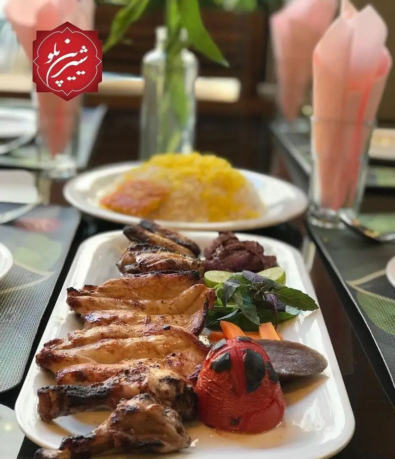 رستوران شیرین پلو: میز غذای ایرانی شامل جوجه کباب لذیذ با برنج زعفرانی و گوجه، مناسب ناهار یا شام در محیطی زیبا و دلنشین.