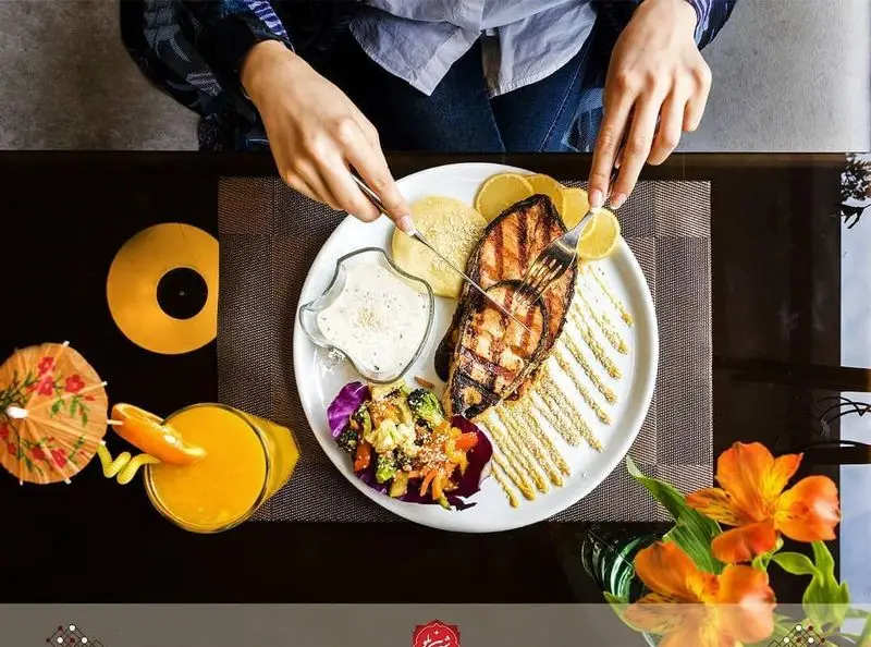 نمایی از غذای دریایی با کیفیت در رستوران شیرین پلو: ماهی گریل، سالاد تازه، سس مخصوص و آب پرتقال، آماده سرو. تجربه لذیذ.