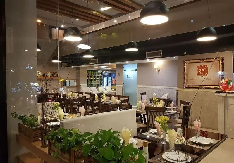 فضای داخلی لوکس و مدرن رستوران شیرین پلو با میز و صندلی‌های چوبی چیده شده، دکوراسیون زیبا و نورپردازی دلنشین آماده پذیرایی.