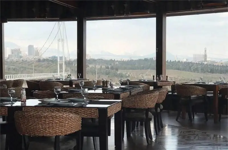 رستوران ایتالیایی مارینو با چیدمان شیک میزها، صندلی‌های حصیری و چشم‌انداز پانورامیک شهر، پل معلق و کوهستان‌های دور.