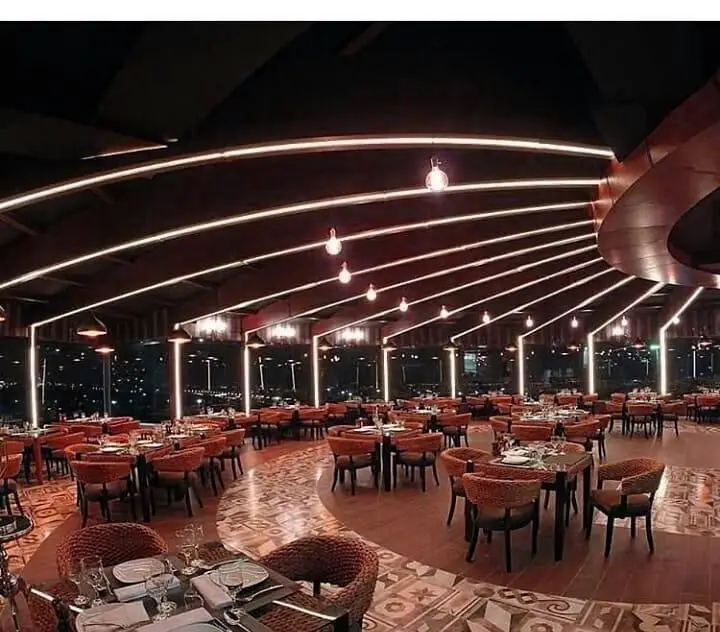 نمایی از فضای داخلی مدرن و لوکس رستوران ایتالیایی مارینو در شب، با سقف منحنی و نورپردازی جذاب، چیدمان میز و صندلی‌های شیک و منظره شهری چشم‌نواز.
