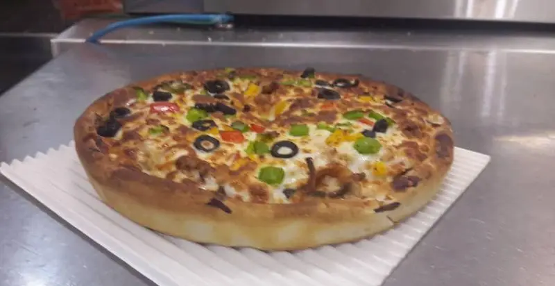 پیتزای لاکچری و خوشمزه با خمیر پفکی و پر از تاپینگ‌های تازه شامل زیتون سیاه، فلفل دلمه ای رنگی و گوشت مرغ در فست فود لاکچری.